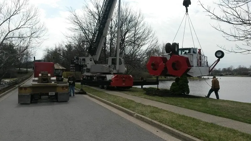 A crane is lifting a large sign on the side of a road.