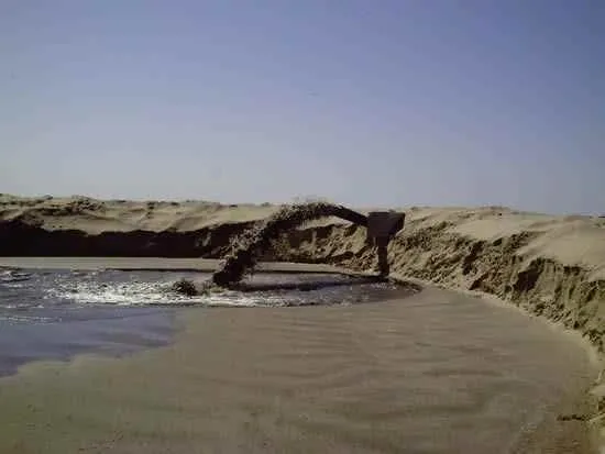 A man is standing in the sand near some water.