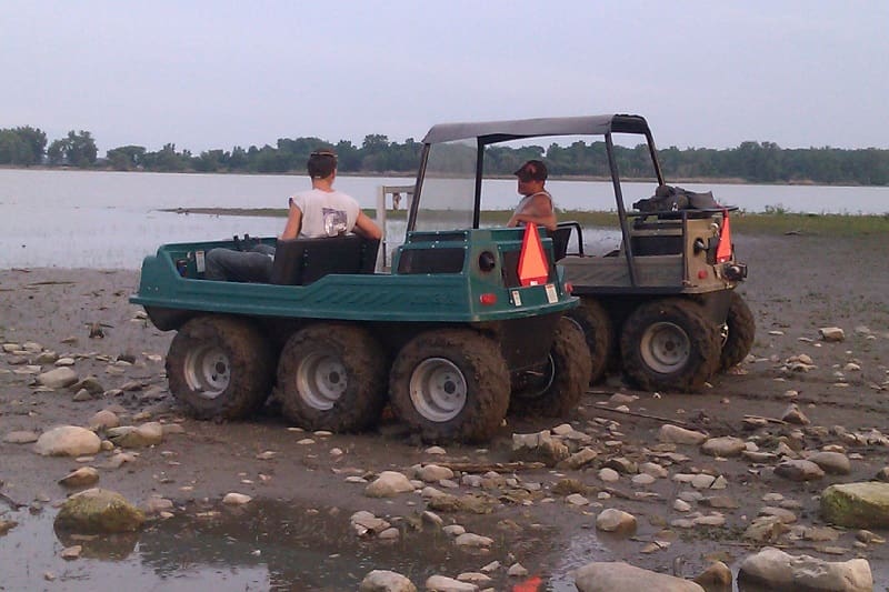 Two people in a green truck on the beach.