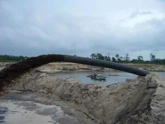 A pipe is in the sand near some water.