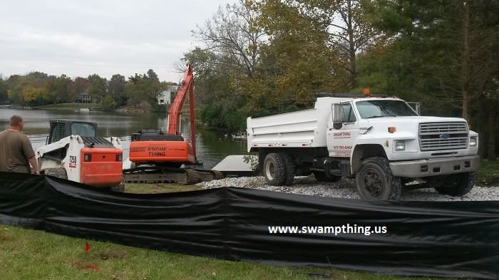 A dump truck is parked next to a large orange and white tractor.